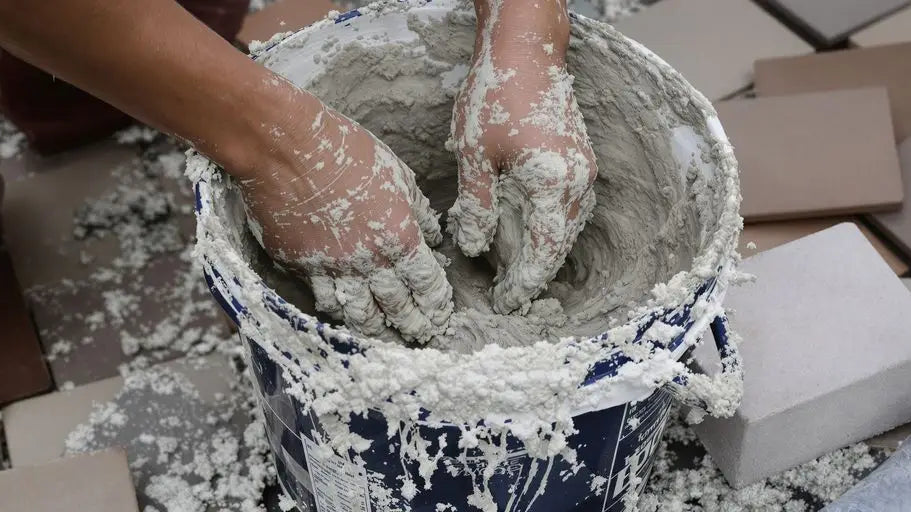 Hands mixing wet grey mortar in blue bucket for outdoor tile projects