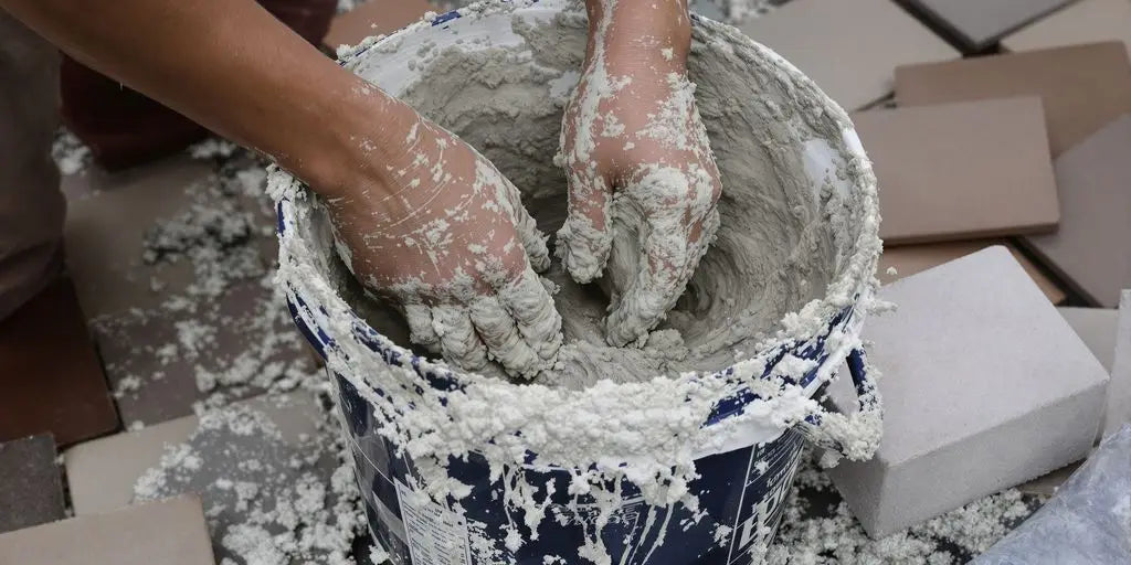 Hands mixing wet grey mortar in blue bucket for outdoor tile projects