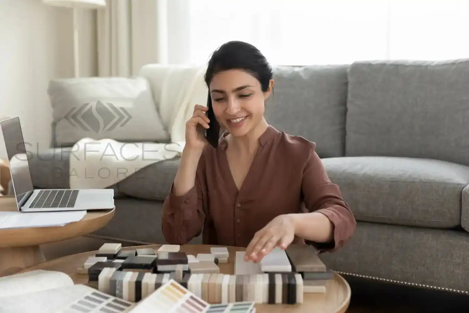 A smiling woman with dark hair talking on a phone and looking at material samples.