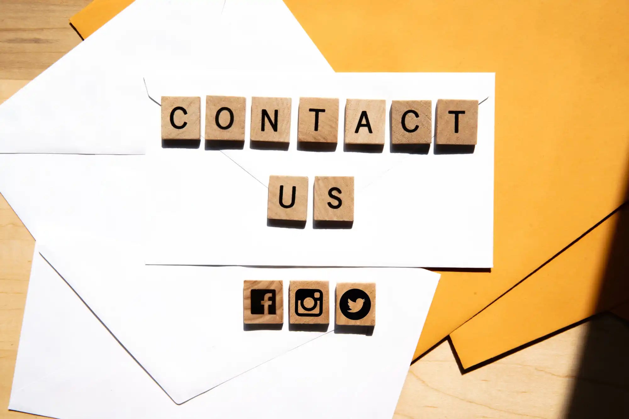 Wooden letter tiles spelling ’CONTACT US’ and social media icons on white envelopes.